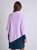 A woman shown from the back wearing a light purple/lavender wrap or poncho over a dark navy dress, against a plain light gray studio background.