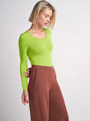 A woman wearing a bright lime green long-sleeve scoop-neck top and high-waisted rust brown wide-leg trousers, photographed against a clean light gray studio background.
