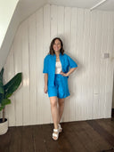 Woman in a blue outfit standing in a room with white paneled walls and wooden floor.