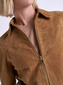 Close-up of a person wearing a tan suede jacket over a light beige knit top, showing the collar, zipper, and textured fabric.