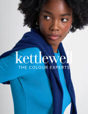 A woman with dark curly hair looks to the side while wearing a bright blue top and a navy blue shawl. Large white text across the center reads 'kettlewell THE COLOUR EXPERTS'.