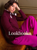 A woman seated on a wooden chair wearing a burgundy zip-front mock-neck sweater over a white collared shirt and bright magenta pants. The word 'Lookbook' is overlaid across the lower center.