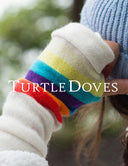 A close-up of a person wearing a white knit sleeve with a rainbow stripe pattern in red, orange, yellow, green, blue, and purple, next to a light blue ribbed knit beanie. The text 'TURTLE DOVES' is overlaid across the center.